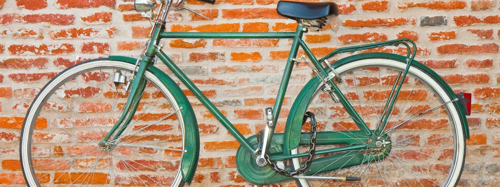 AdobeStock_220772261_Old green bicycle parked against a brick wall