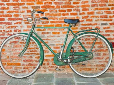 AdobeStock_220772261_Old green bicycle parked against a brick wall